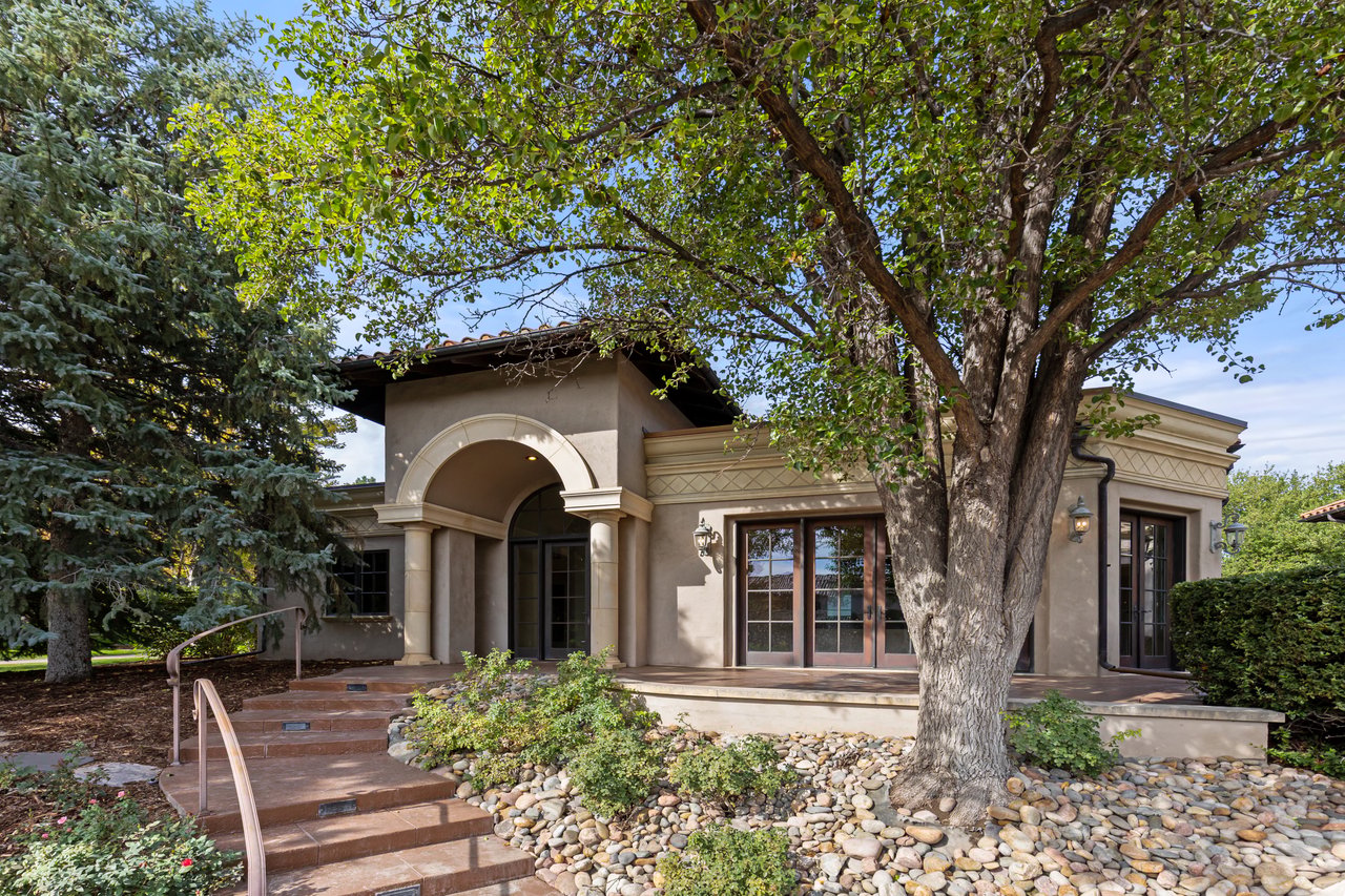 Tan stucco estate with an arched entry, broad steps, and mature trees in the garden.
