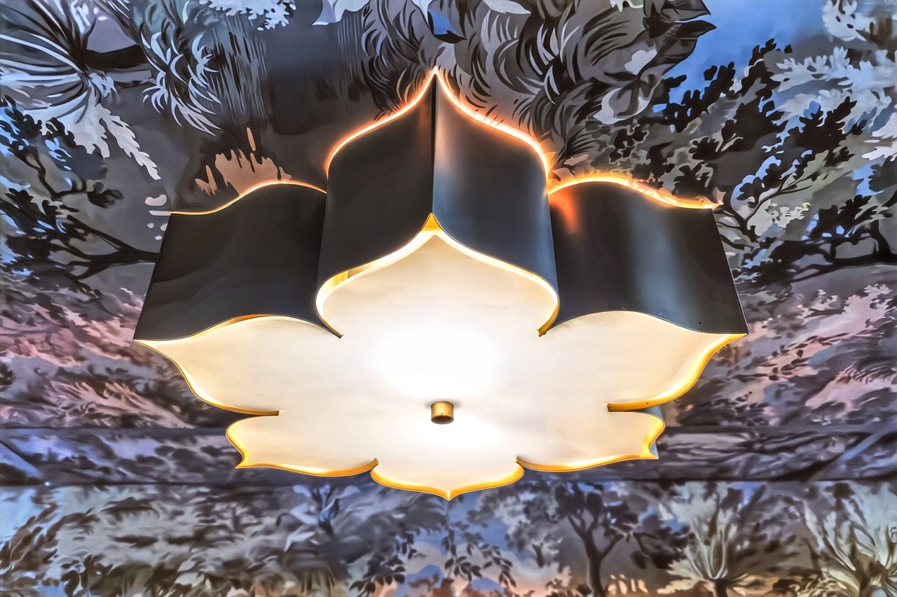 Sculptural pendant light with gold trim beneath an ornate floral ceiling.