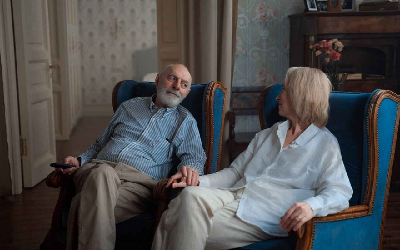 Older couple relaxing together in blue armchairs in a traditional living room.