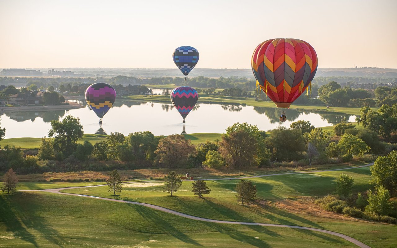 Colorful hot air balloons float above a lake and green golf course.