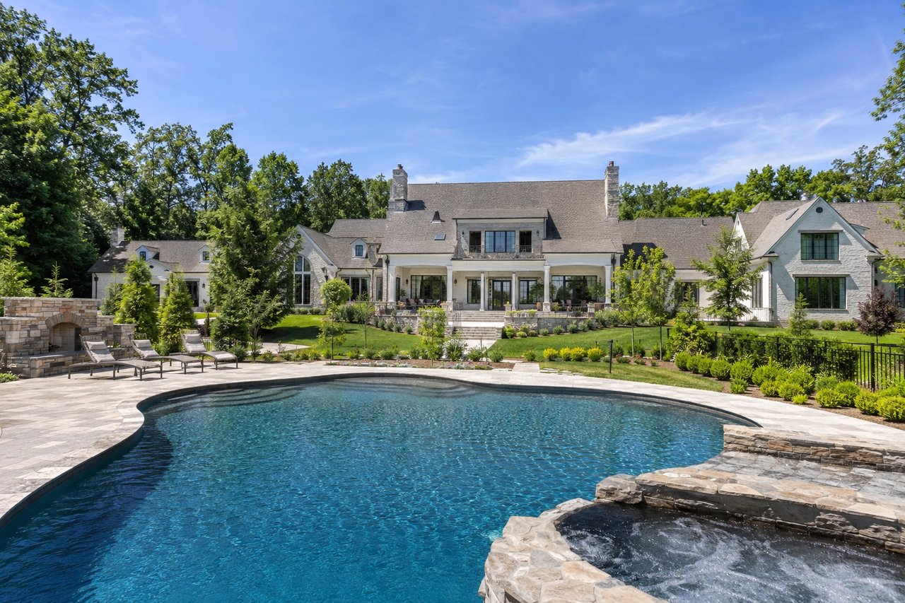 Luxury Nashville estate on expansive acreage featuring a custom-built home, resort-style swimming pool, manicured landscaping, mature trees, and spacious private grounds in Middle Tennessee under a clear blue sky.
