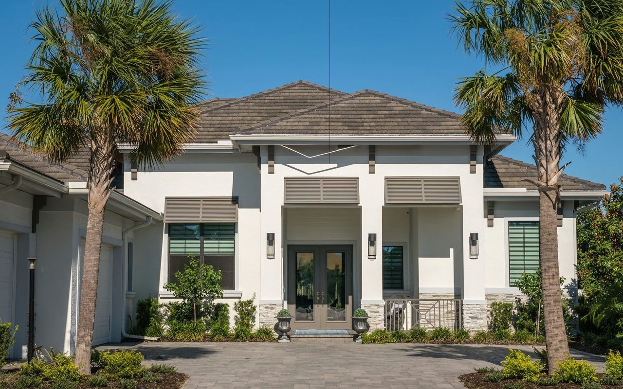 White stucco home with a covered entrance and palm trees beside the paved drive.