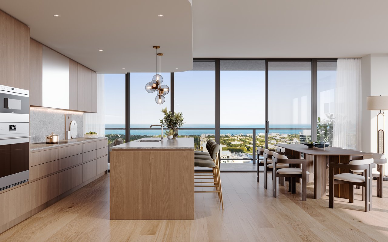 Modern condominium kitchen with a wood island and dining area overlooking the ocean through floor-to-ceiling windows.