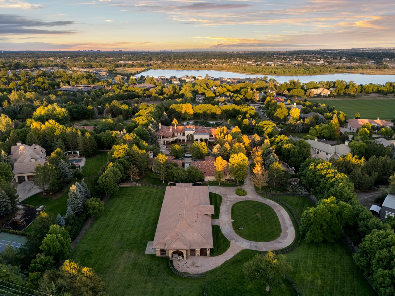 Aerial view of an equestrian estate with a red-roofed barn, fenced pastures, and a lake on the horizon.