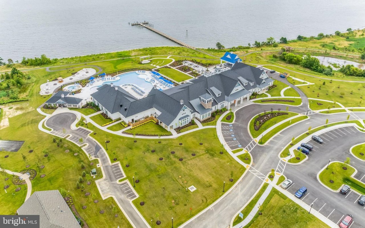 Waterfront clubhouse with a swimming pool, landscaped grounds, and a pier seen from above.