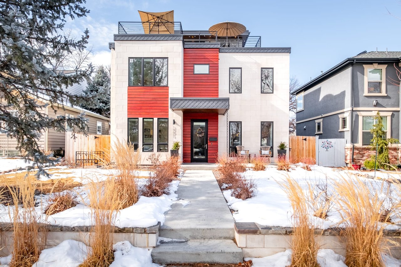 Modern house with rooftop patio, light stucco, dark wood trim, palm trees, and glass railing.