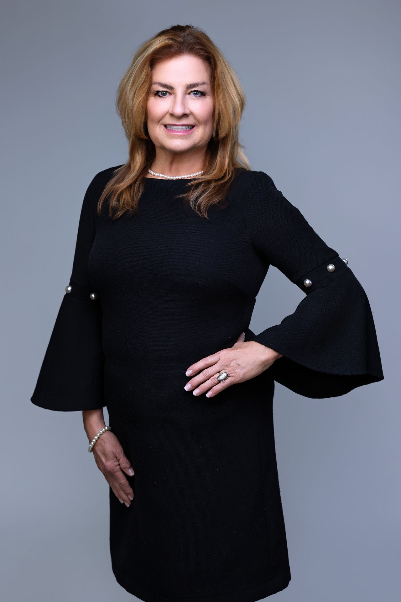 Ginger Delong in a black dress with flared sleeves and pearl jewelry