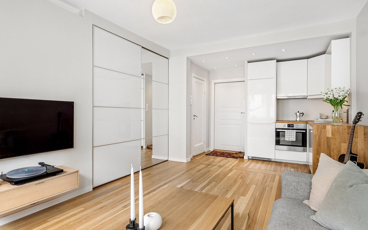 Open-plan living room and kitchen with white cabinetry, wood floors, and a gray sofa.