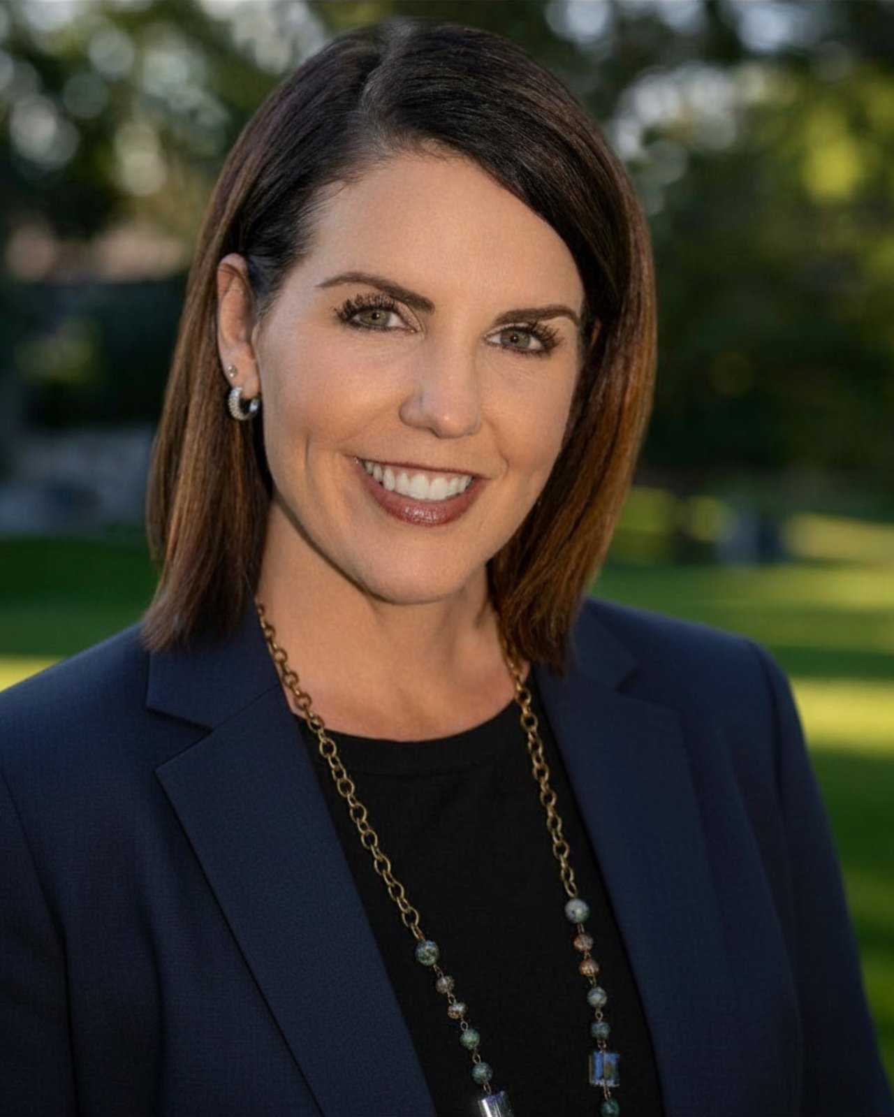 Andrea Wright smiling in a navy blazer and long beaded necklace.