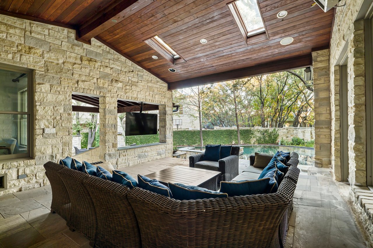 Covered patio outdoor living room with stone columns, wood plank ceiling, and skylights at 5902 Saratoga Cove, Davenport Ranch, Austin, Texas.