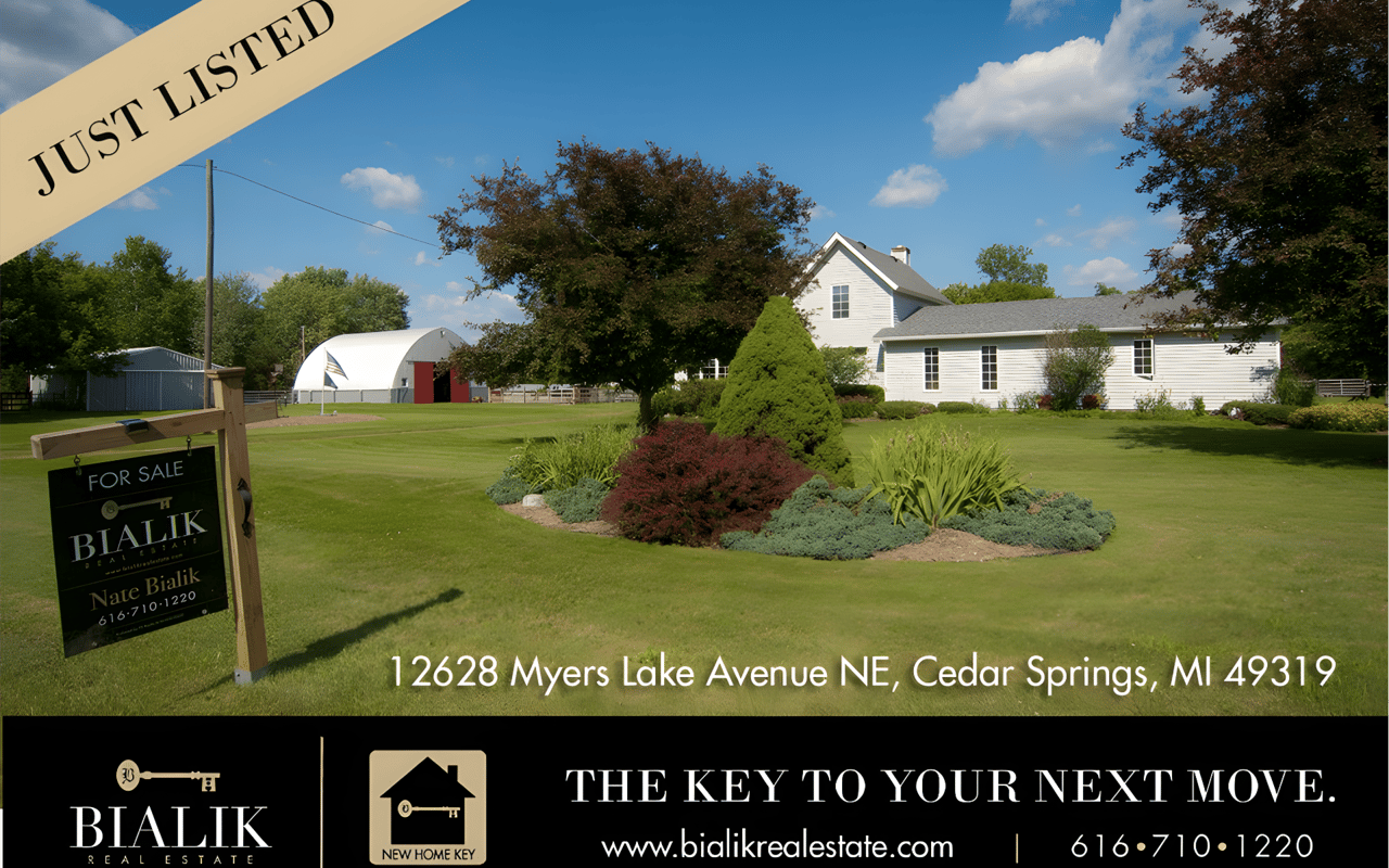 White farmhouse and outbuildings across a landscaped lawn, with a Bialik Realty for-sale sign.