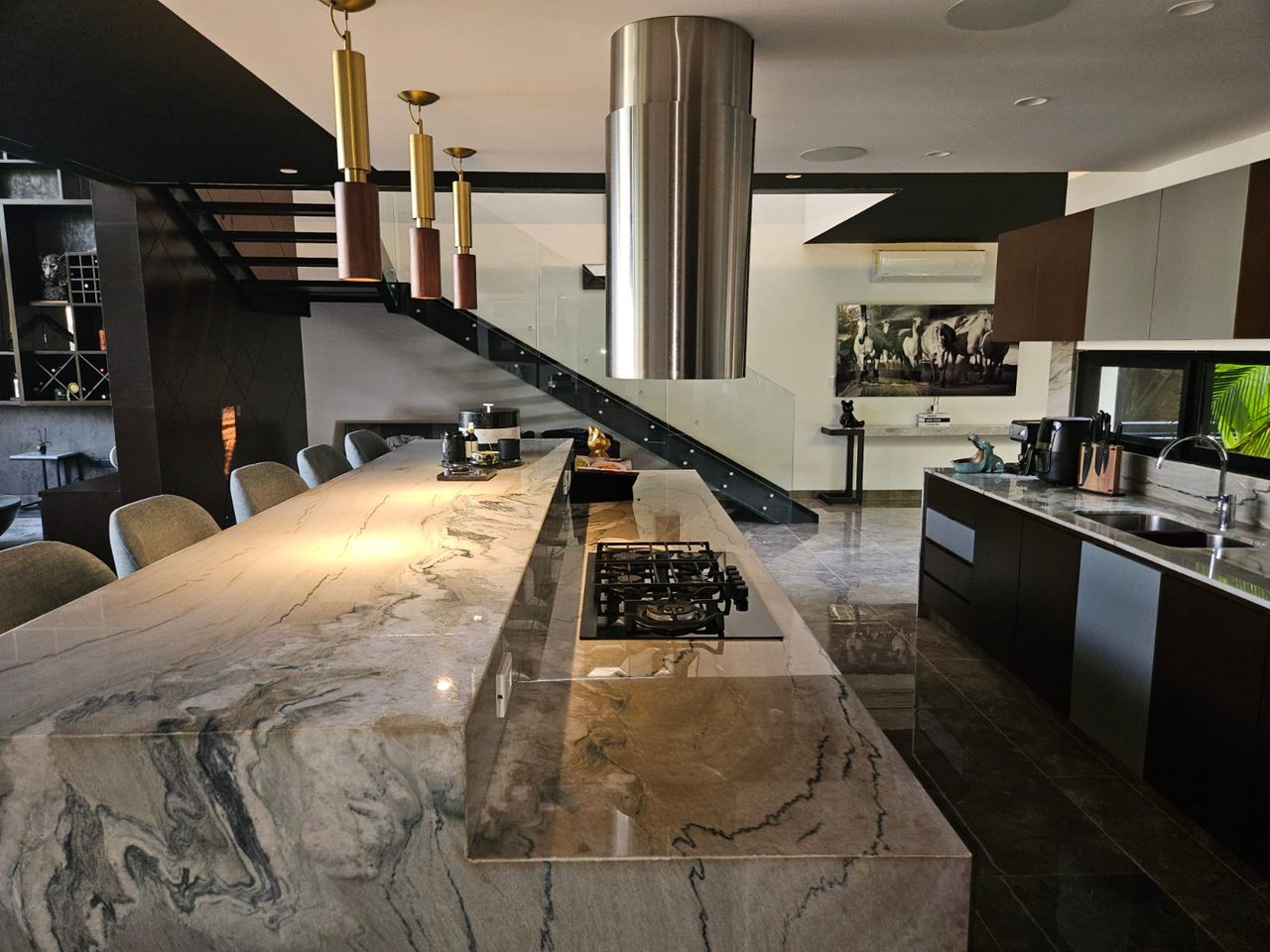 Modern kitchen with a veined marble island, built-in cooktop, and glass-railed staircase.