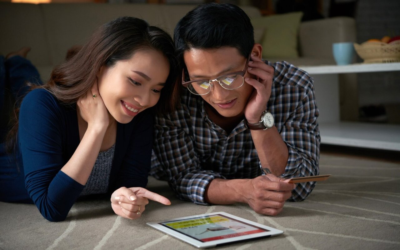 Couple reviews a tablet and card together on a living-room floor.