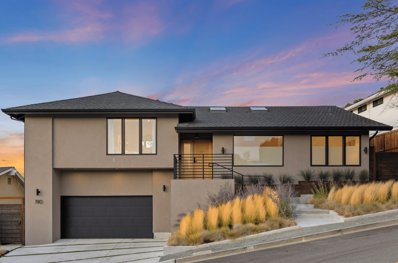 Modern two-story home at dusk with black-framed windows and ornamental grasses along the front steps.