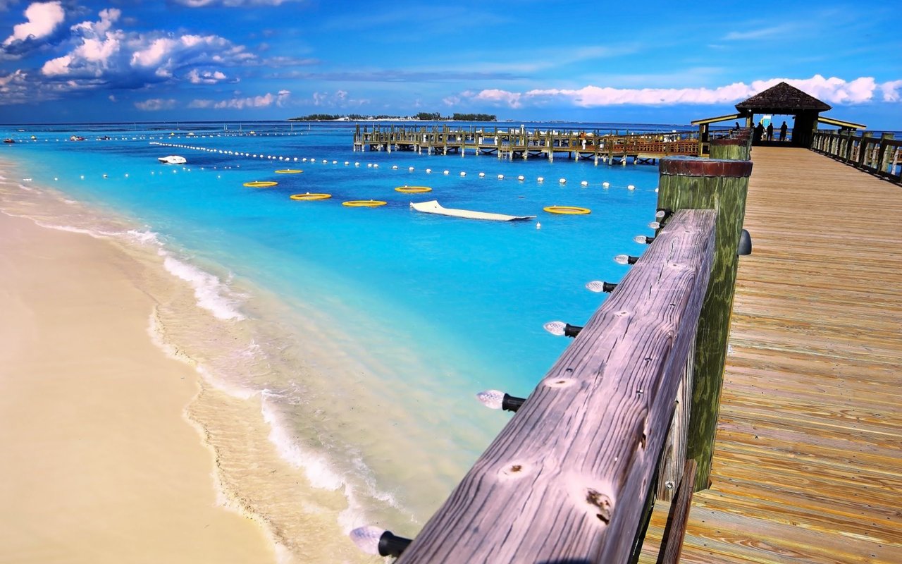 Cable Beach shoreline with turquoise water, swim buoys, and a wooden pier.