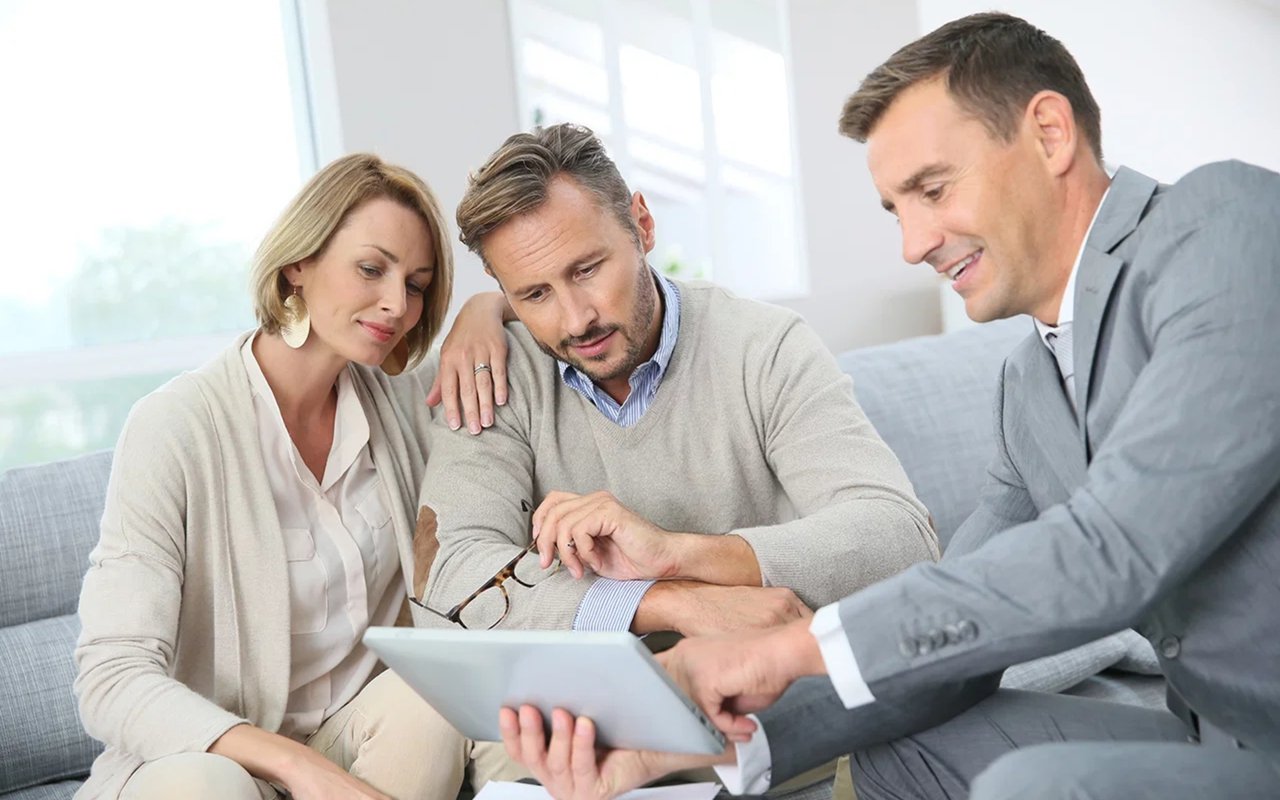 Real estate agent reviews a tablet with a couple seated beside him.