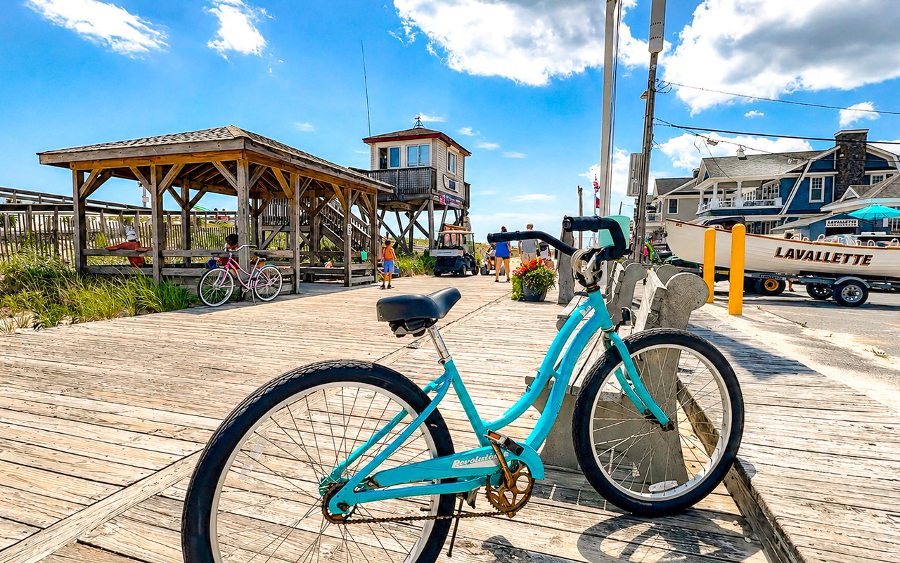 Turquoise bicycle on a Lavallette boardwalk beside a wooden pavilion and a boat marked “LAVALLETTE.”