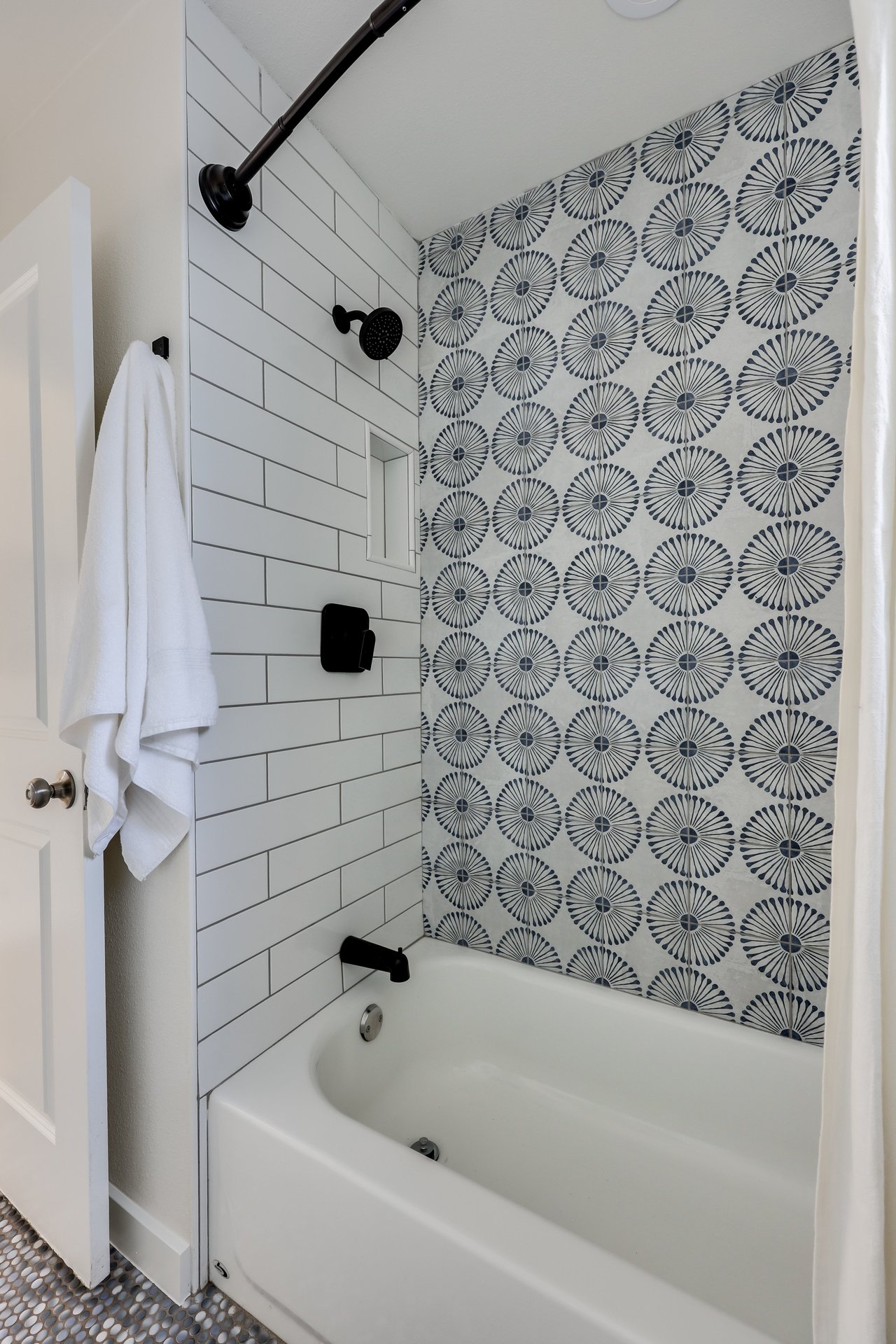 Bathroom tub and shower with patterned accent tile, white subway tile, and matte black fixtures.
