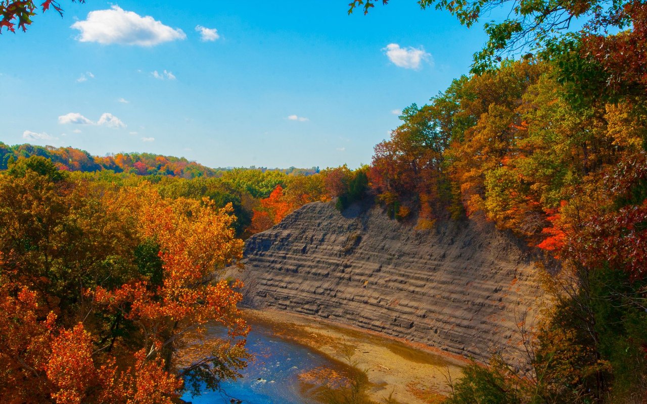 Rocky River gorge with exposed layered rock and colorful autumn trees.