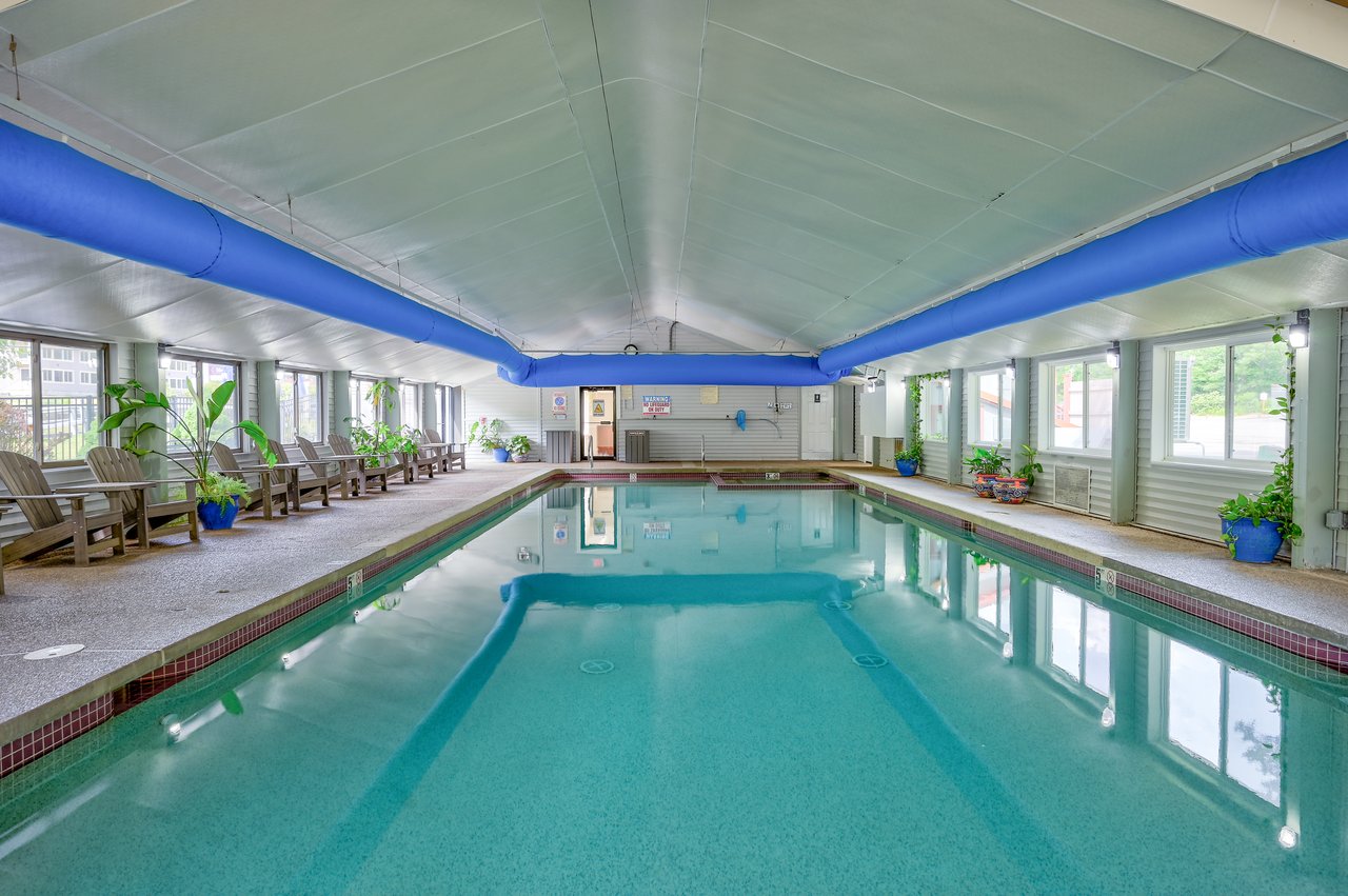 Indoor pool with a blue ceiling duct and lounge chairs along the deck.