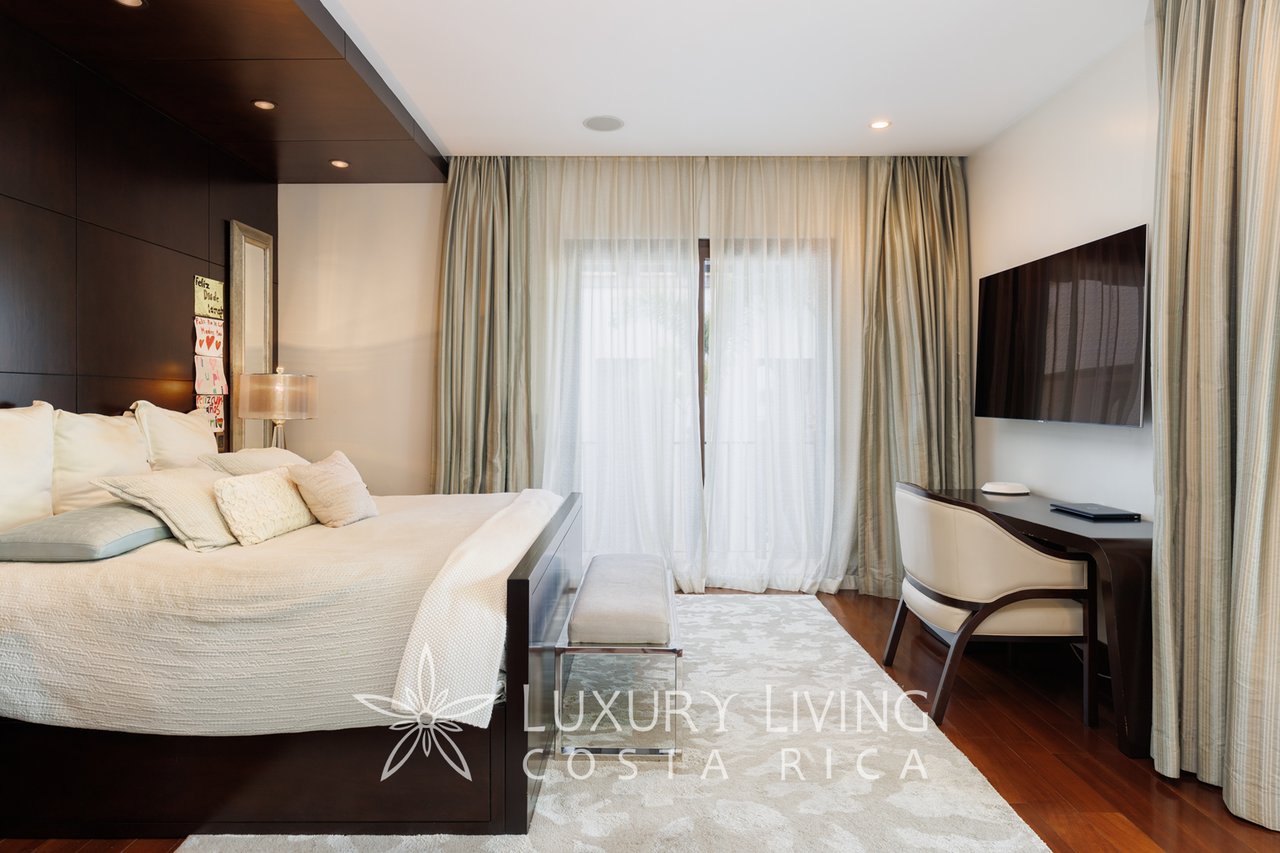 Bedroom with a large white bed, dark wood headboard, floor-to-ceiling curtains, and a television.