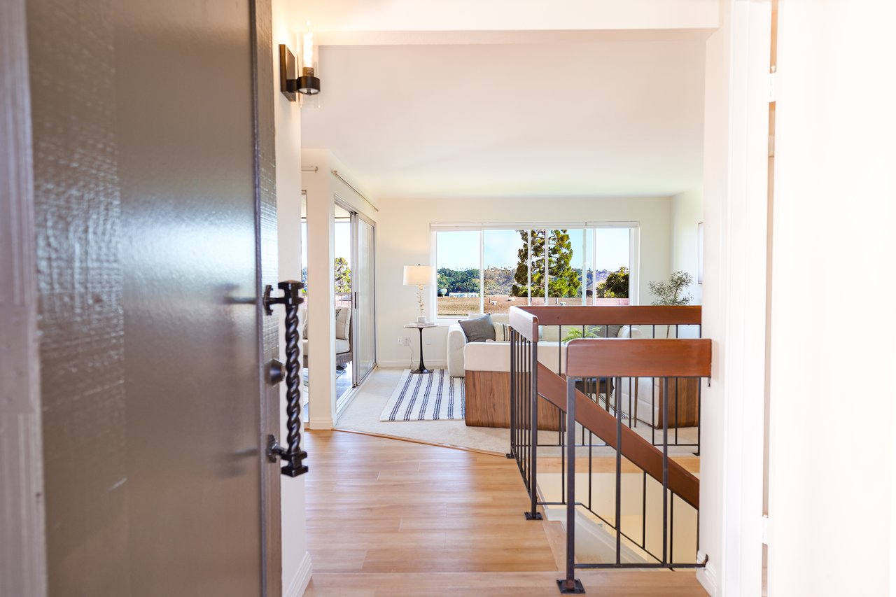 View from entryway into the living room at 6321 Caminito Luisito townhome in San Diego, CA 92111, featuring natural light, large windows, sliding glass doors, and open floor plan.