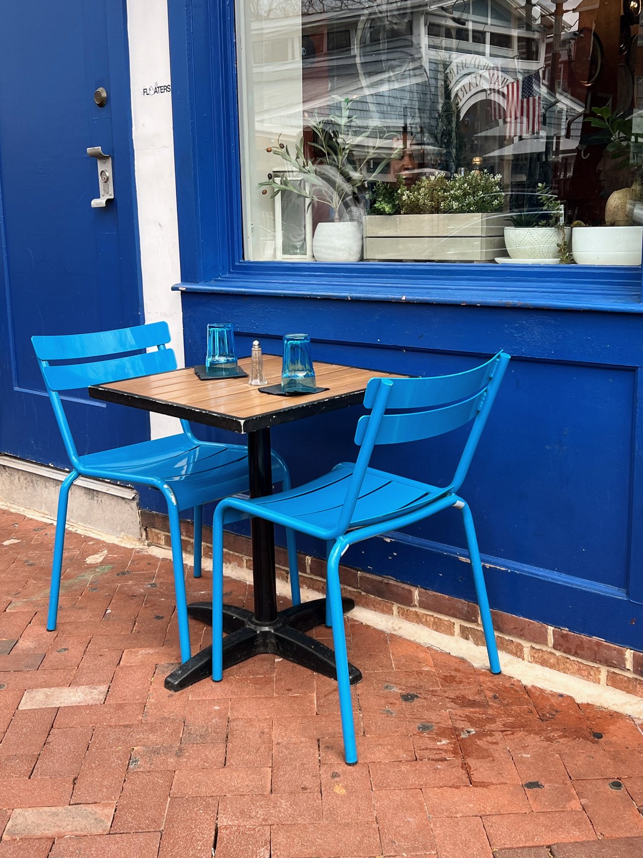 Restaurant patio with bright blue chairs and a wooden table beside a blue storefront.