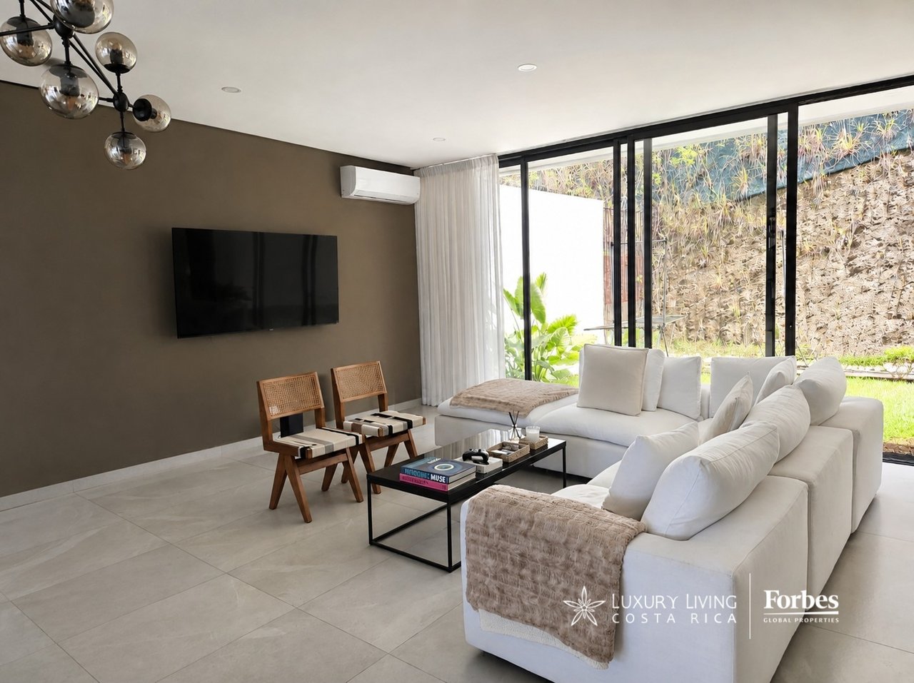 Contemporary living room with a white sectional, wooden chairs, and floor-to-ceiling glass doors.