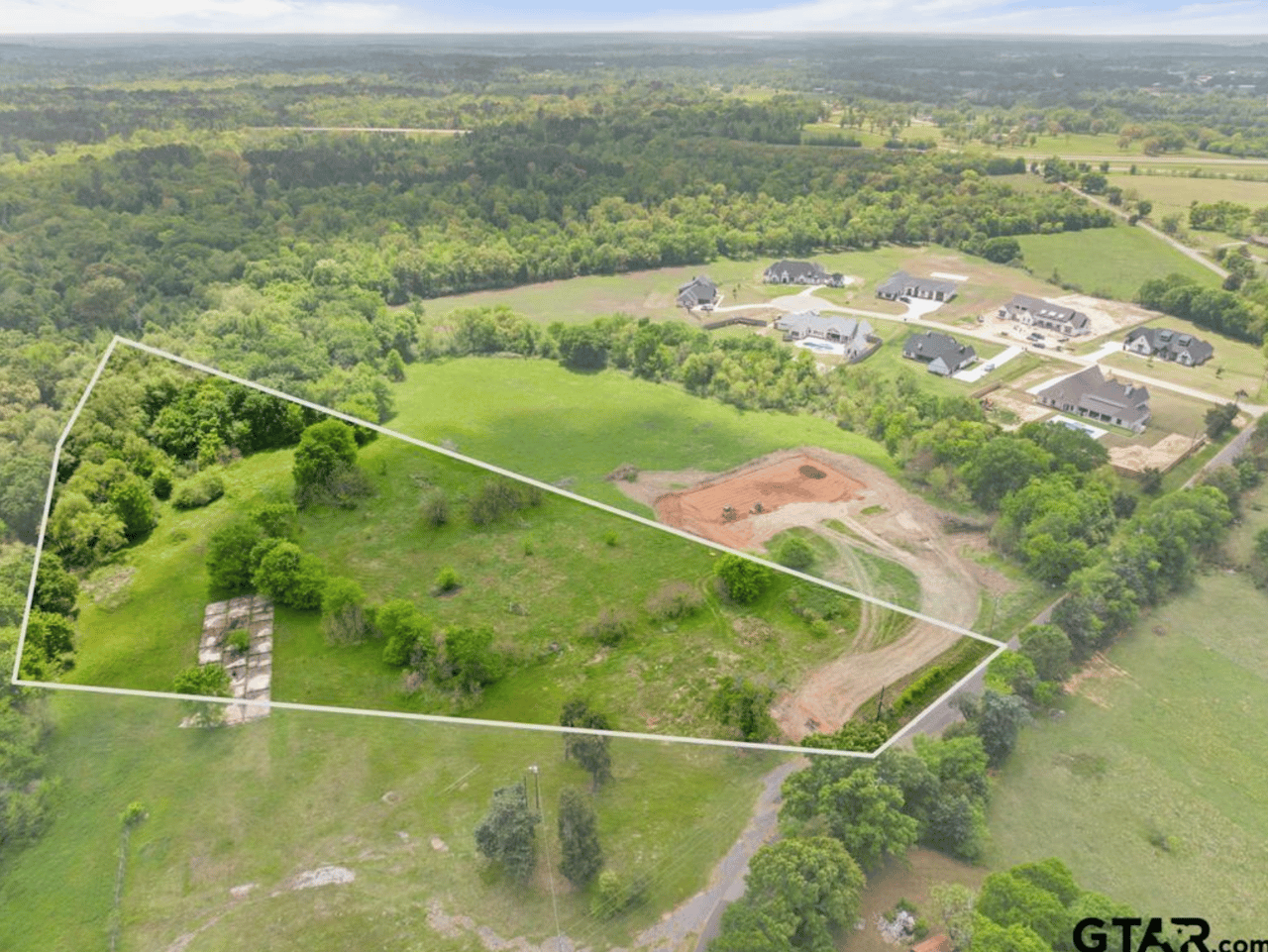 Alt text: "Aerial view of 5.98-acre open land lot for sale at 15627 CR 192 in Thedford Farms, Tyler TX, with property lines marked, open pasture, and new construction homes nearby — East Texas acreage for sale.