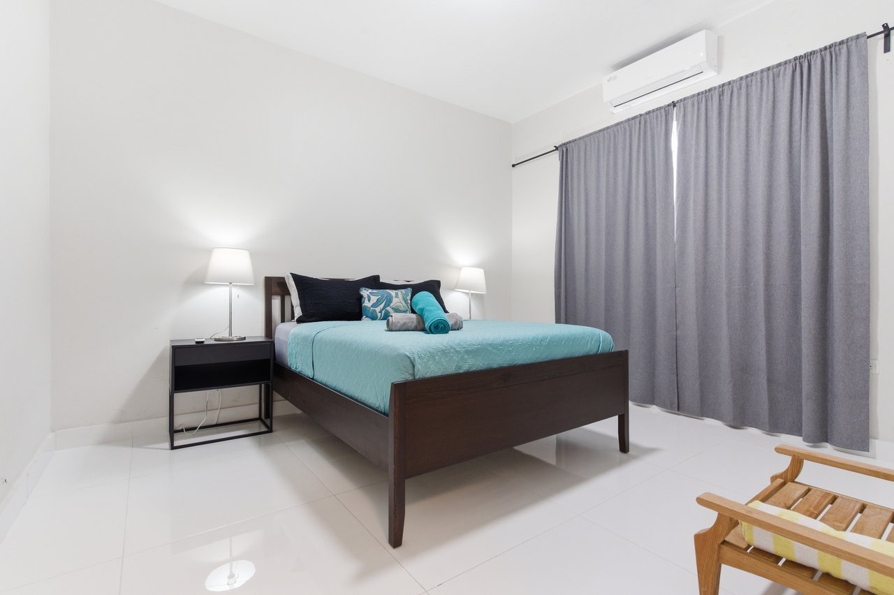 Furnished bedroom with turquoise bedding, gray curtains, and a wall-mounted air conditioner.