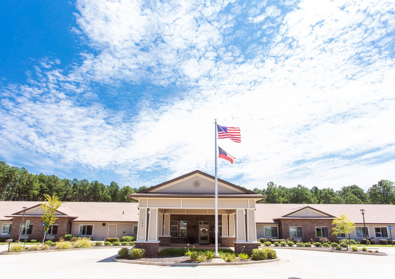 Senior living community entrance with brick facade, landscaped grounds, and American and Georgia flags.