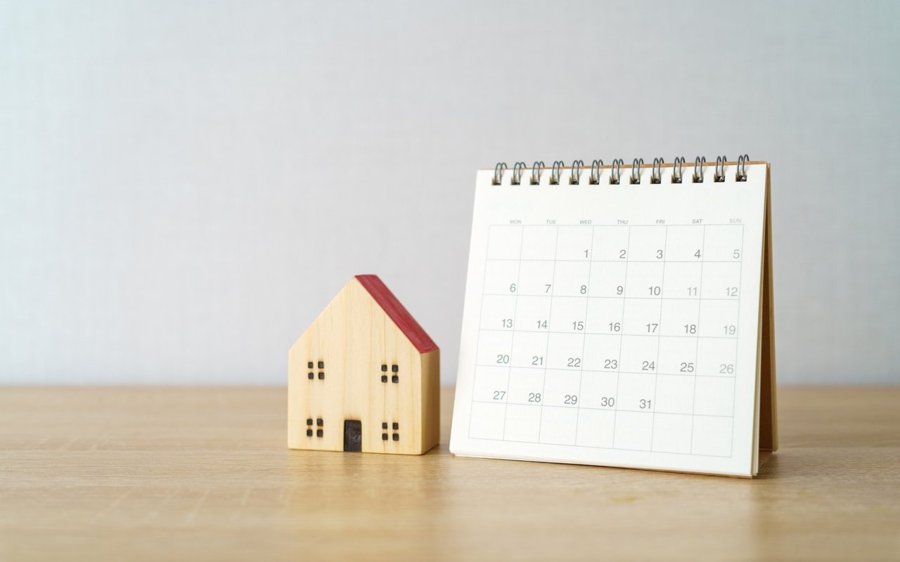 Wooden model house beside a desk calendar, illustrating days on the market.