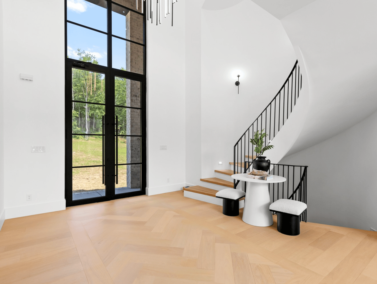 Modern foyer with a sweeping black-railed staircase and tall glass entry doors.