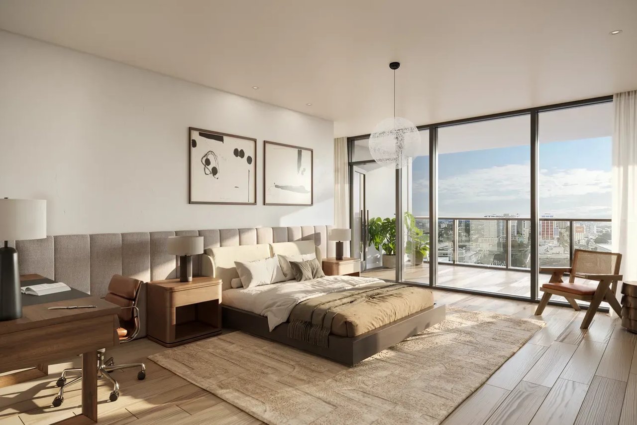Modern bedroom with a low bed and balcony doors overlooking the city skyline.