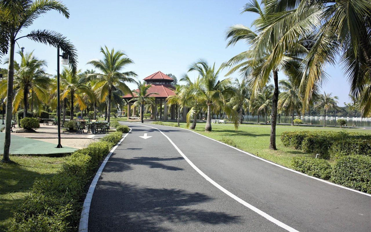 Palm-lined park path leading to a red-tiled gazebo beside a lake