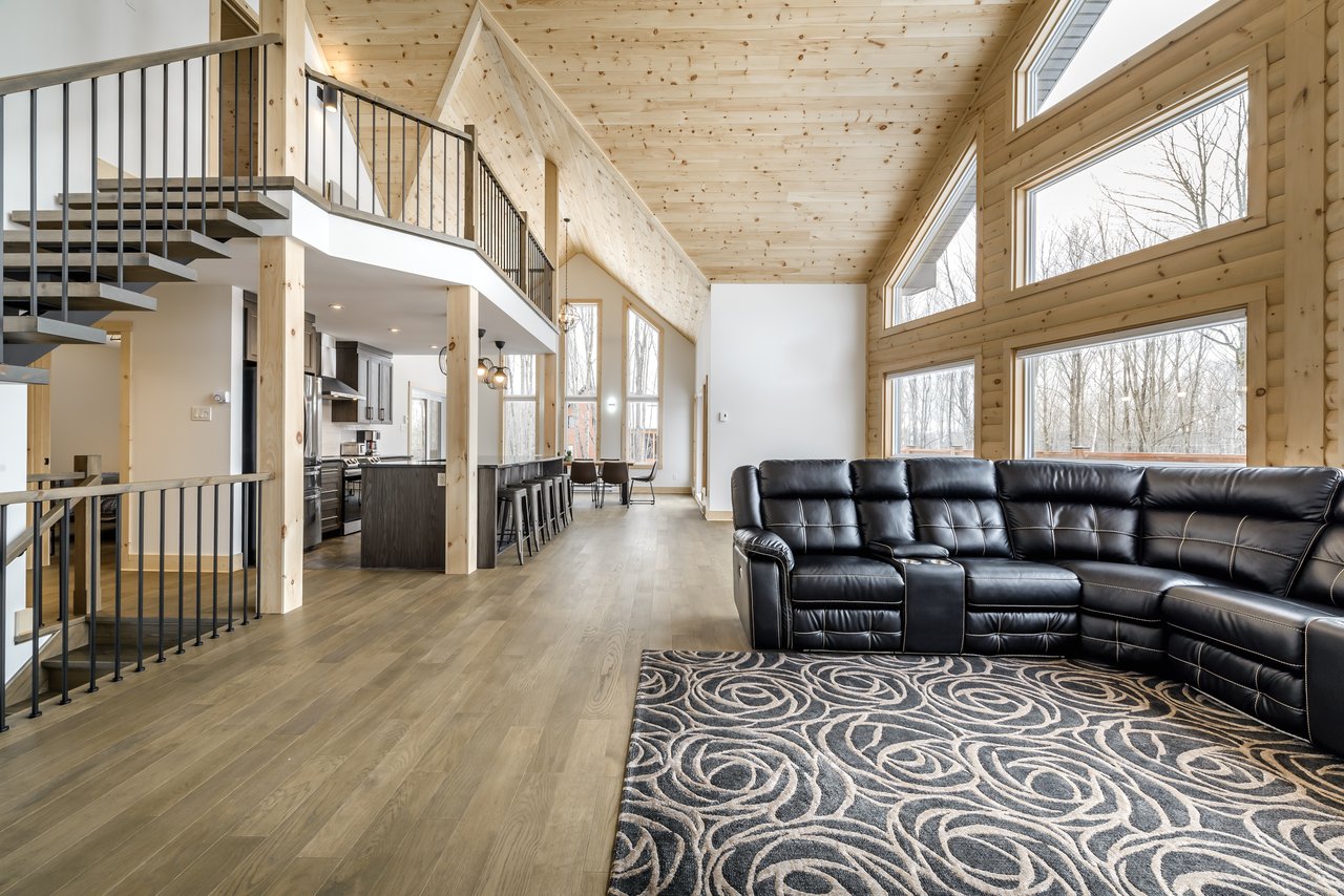 Open-plan living room with vaulted wood ceiling, tall windows, and black leather sectional.