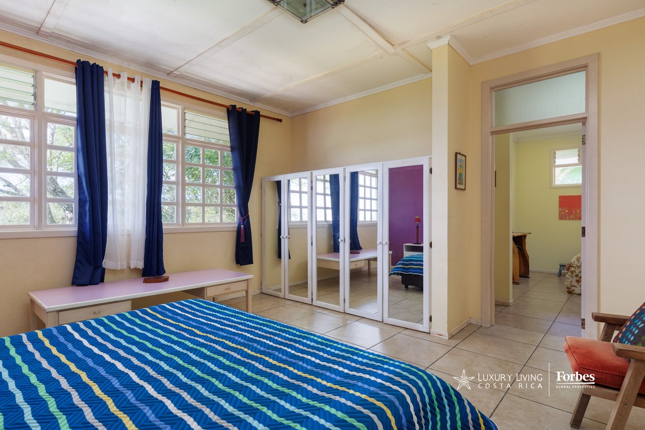 Bedroom with a blue striped bedspread, large curtained windows, and mirrored wardrobe doors.