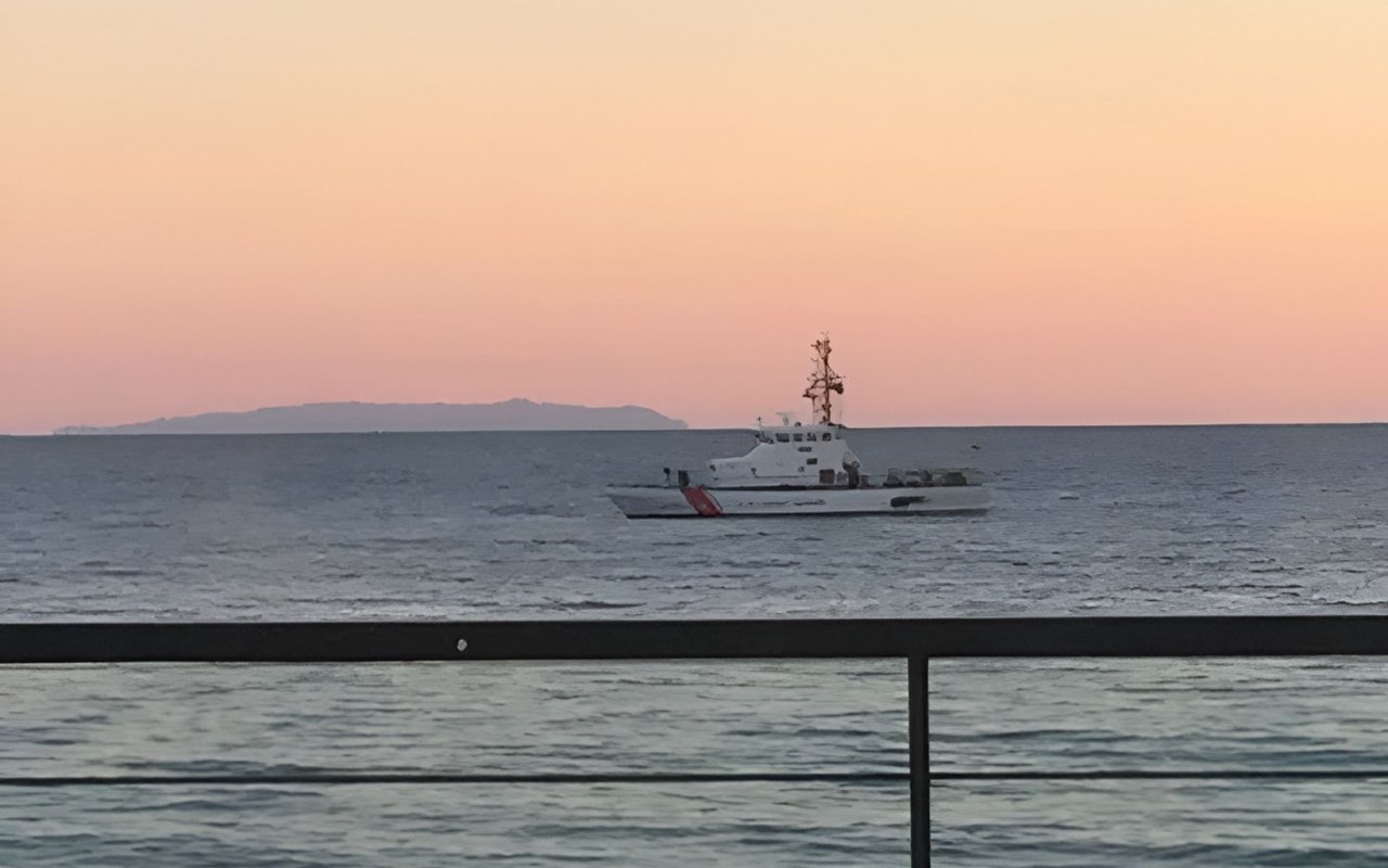 Ocean at dusk with a white boat offshore, seen over a dark railing.