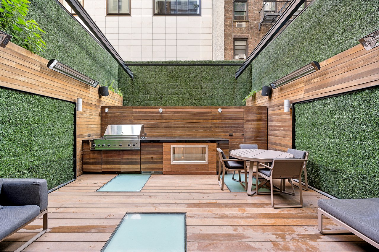 Rooftop terrace with a built-in grill, dining table, and tall green walls.
