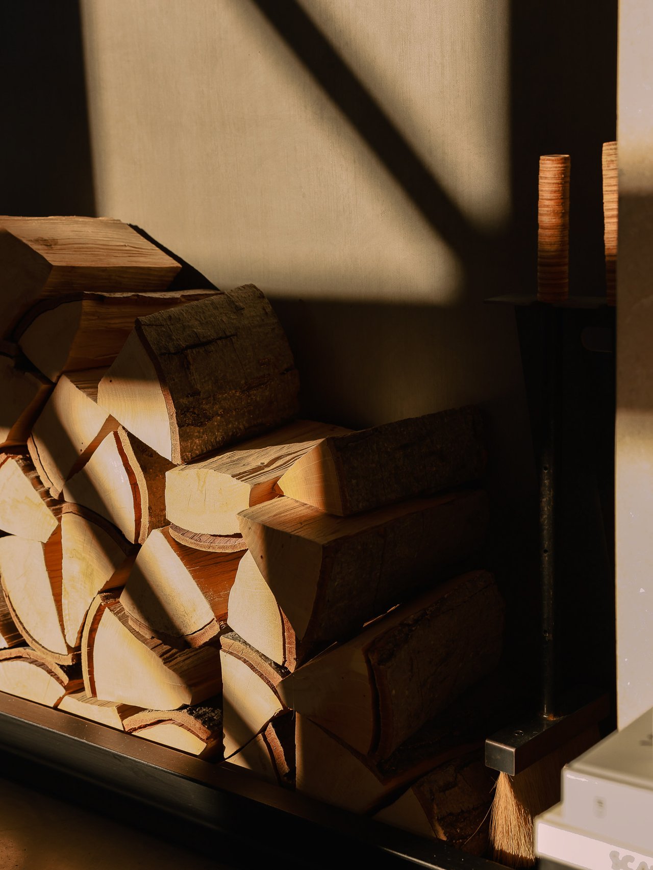 Stacked firewood inside a dark fireplace, illuminated by warm sunlight.