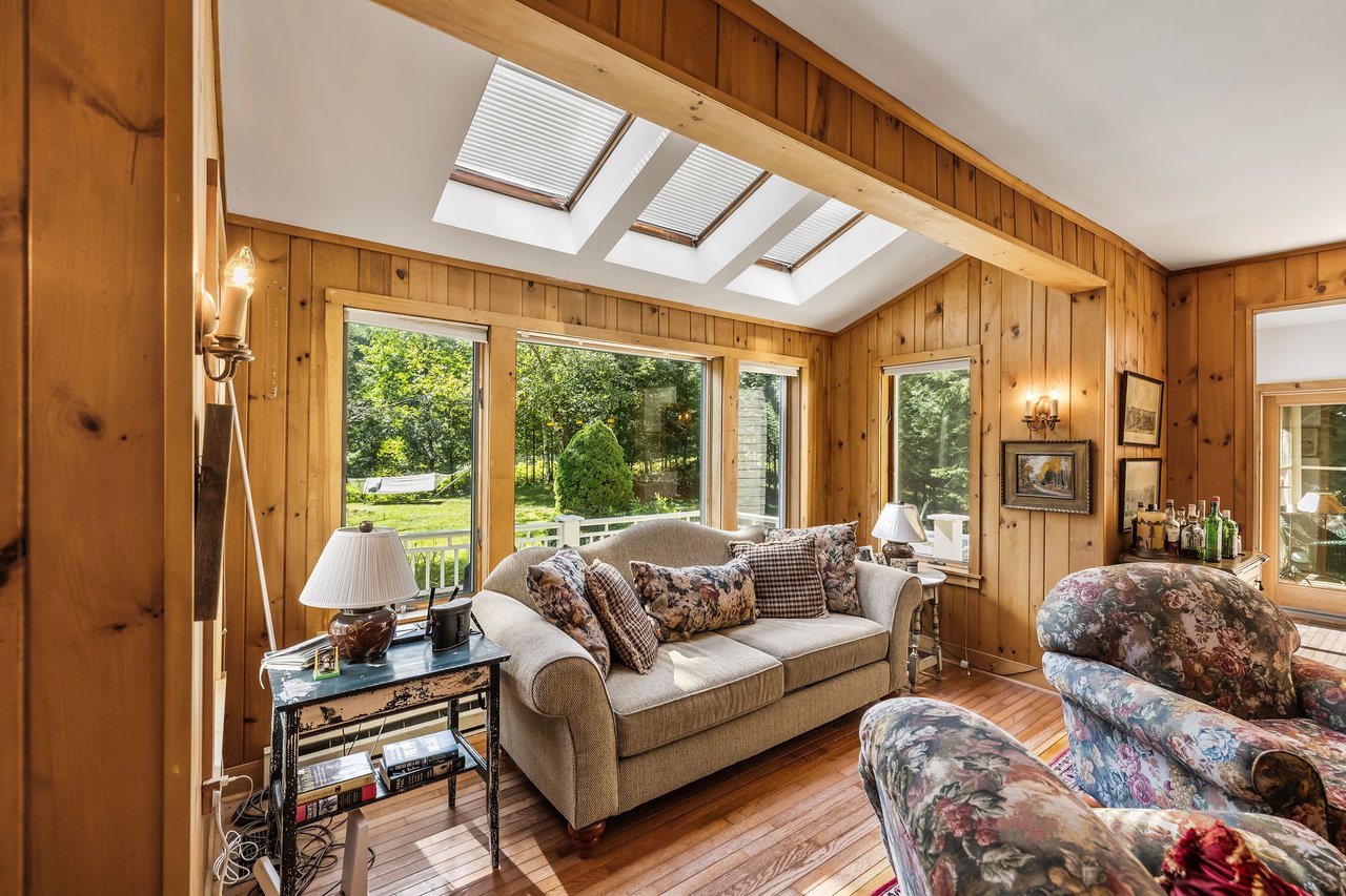 Living room with pine walls, three skylights, broad windows, hardwood floors, and floral armchairs.
