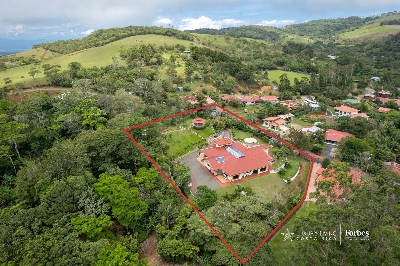 Aerial view of a red-roof mountain home and marked property amid green hills.