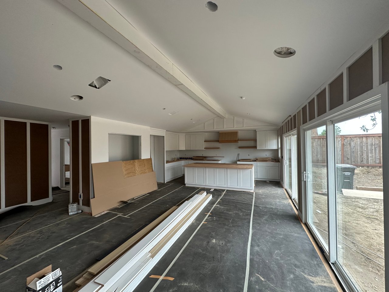 Kitchen under renovation with white cabinets, a large island, and sliding glass doors to a fenced yard.