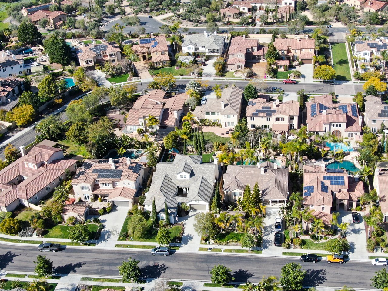 Aerial neighborhood of detached homes with tiled roofs, pools, and rooftop solar panels.