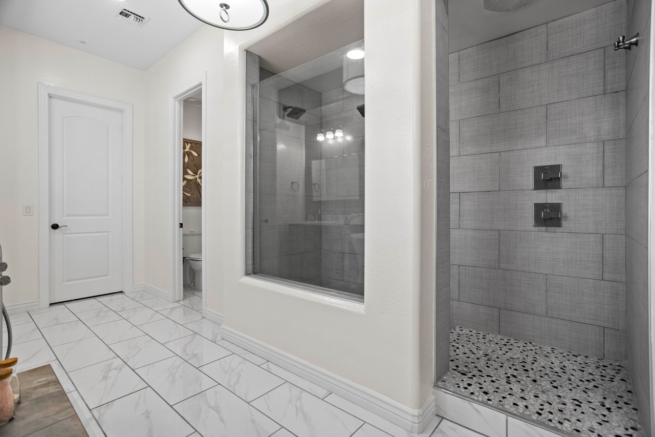 Bright bathroom with large tiled double shower, glass partition, white tile floor, and a separate toilet room doorway.