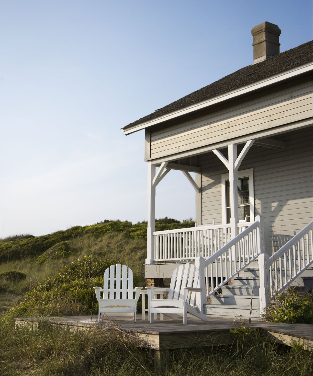 House porch with white railings and chairs beside grassy dunes.