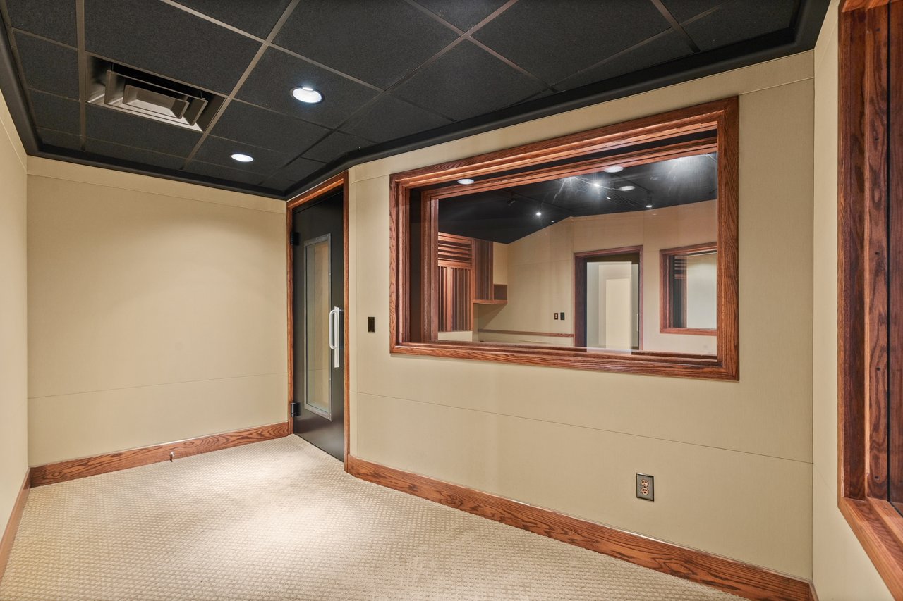 Empty recording room with a large wood-trimmed window into an adjoining room.