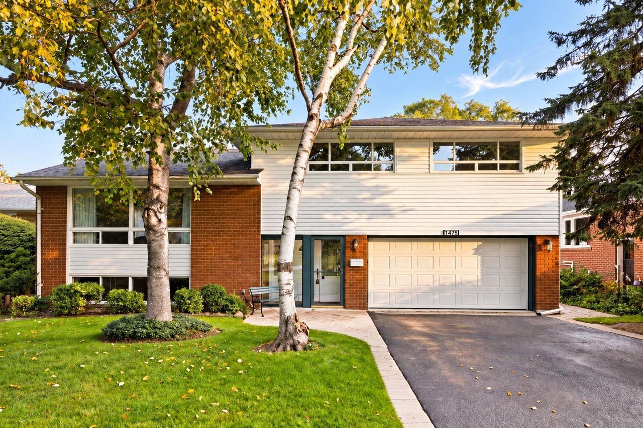 Split-level home with red brick, white siding, a double garage, and mature trees in the front yard.