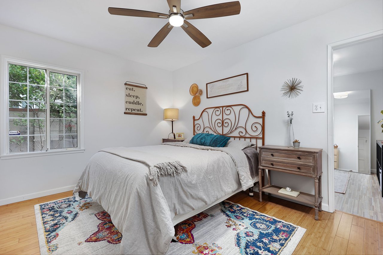 Serene primary bedroom with large window, ceiling fan, neutral tones, and bamboo flooring