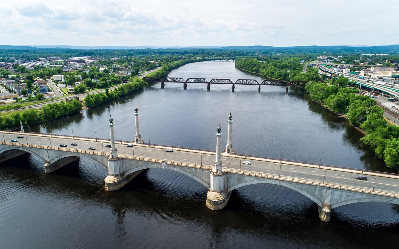 Aerial view of two bridges crossing a wide river, with green neighborhoods along the banks.